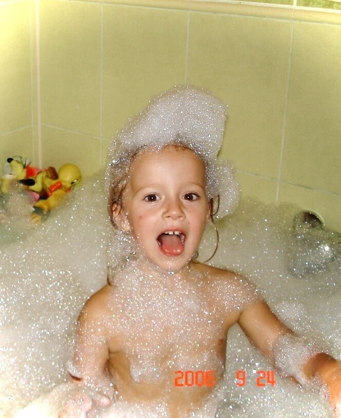 Veronica as a child, laughing in a bubble bath